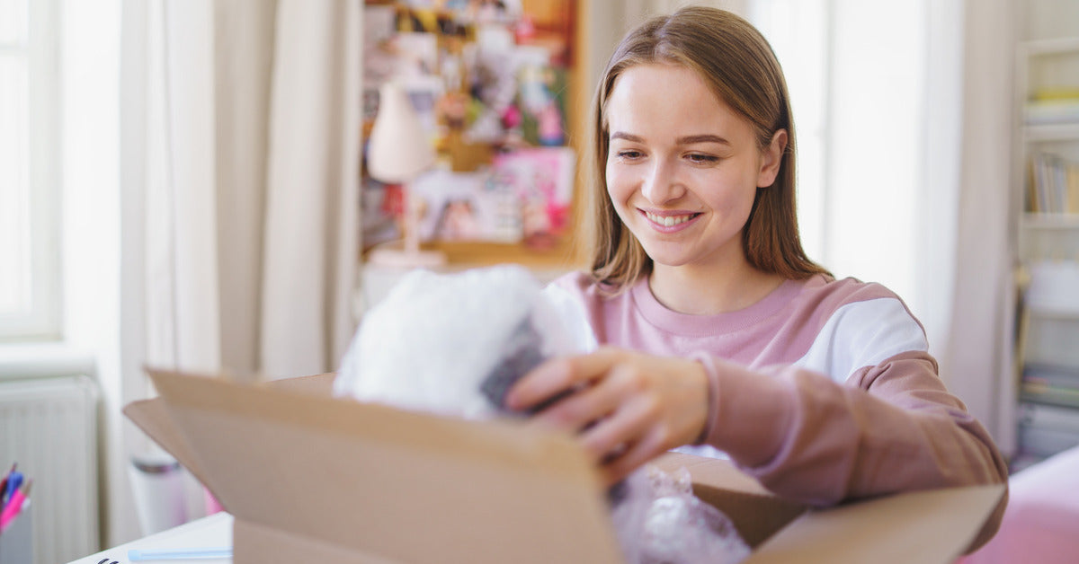 A young woman opens a package on her desk. She's smiling and pulling out items from the box.