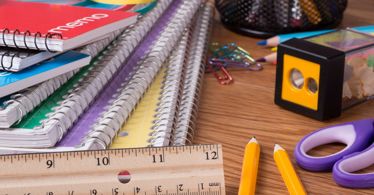An assortment of school supplies, including notebooks, pencil sharpeners, and a ruler, sits on a wooden desk.