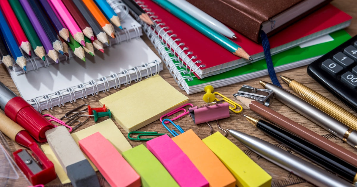 Various office supplies, including notebooks, sticky notes, paper clips, pens, pencils, and sharpeners, sit on a desk.