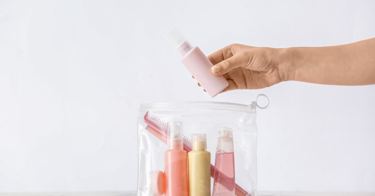 Someone's hand is placing a travel size toiletries into a clear bag with a comb on clean white background.