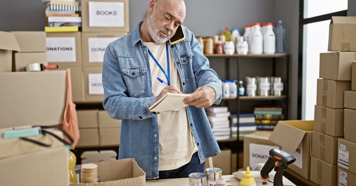 A volunteer reviews a checklist while organizing boxes and bulk supplies for an upcoming community donation effort.