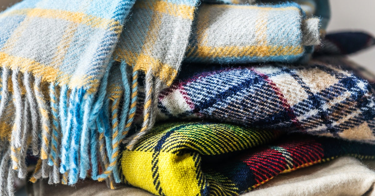 A close-up of wool blankets stacked on each other. Each blanket has a checkered pattern, and the top one has fringe.