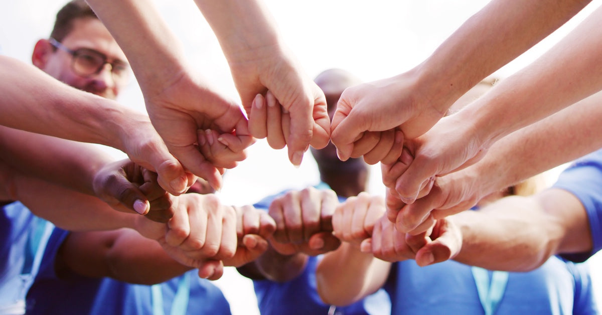 A group of people in matching blue shirts stand in a circle, touching fists to show unity and encouragement.