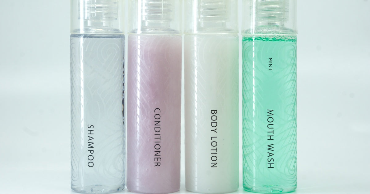 Identical containers of shampoo, conditioner, lotion, and mouthwash are lined up, each in a different color.