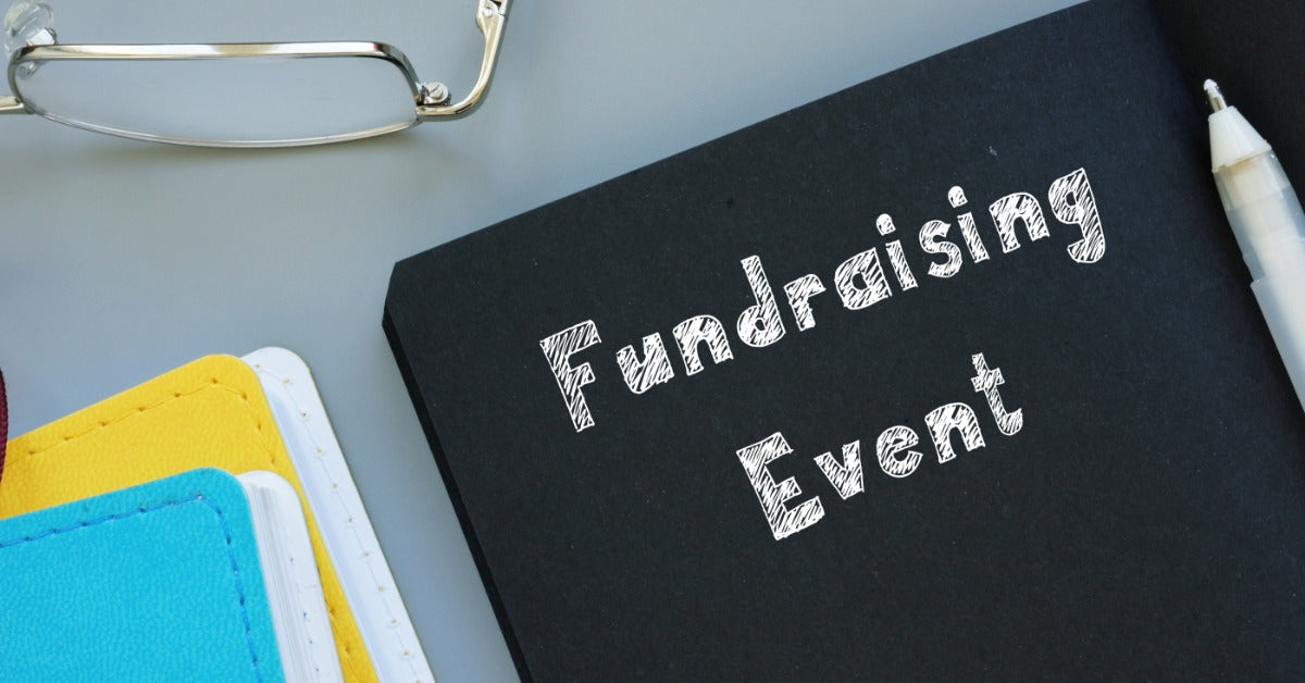 A notebook labeled “Fundraising Event” lies on a desk beside eyeglasses, a pen, and colorful folders.