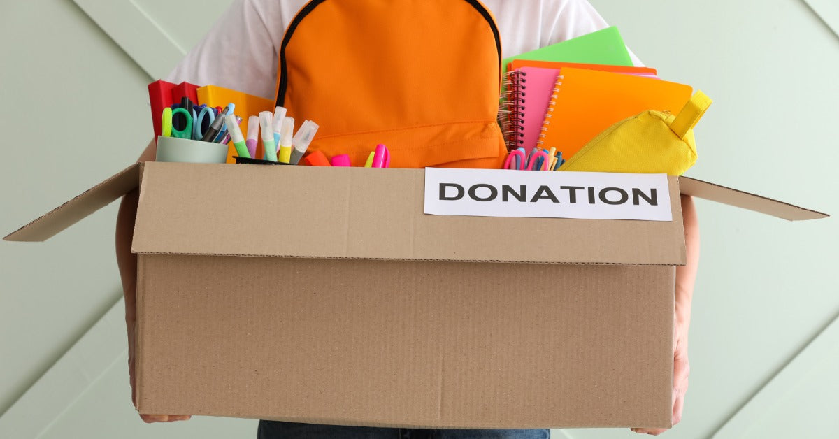 A donation box is filled with school supplies like notebooks, markers, and a backpack for student support programs.