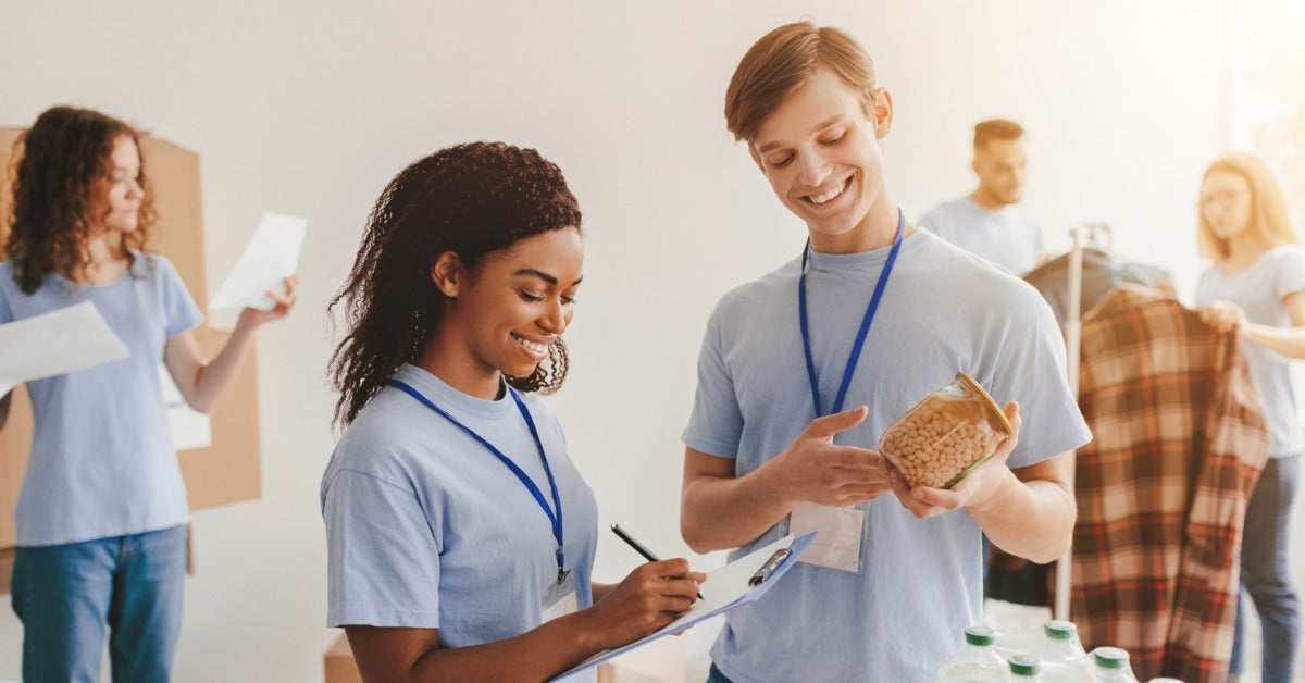 A volunteer reviews donated supplies on a clipboard while another volunteer holds a packaged food item.